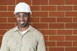 Photo: Portrait of happy young construction worker with hardhat over brick wall Portrait of happy young construction worker with hardhat over brick wall