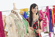 Photo: Pretty Indian female dressmaker looking away while working on traditional outfit Pretty Indian female dressmaker looking away while working on traditional outfit