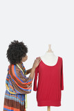 Photo: African American female fashion designer looking at red tunic over gray background African American female fashion designer looking at red tunic over gray background