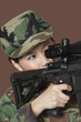 Photo: Young female US Marine Corps soldier aiming M4 assault rifle over brown background Young female US Marine Corps soldier aiming M4 assault rifle over brown background