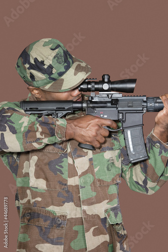 Photo: Male US Marine Corps soldier aiming M4 assault rifle over brown background Male US Marine Corps soldier aiming M4 assault rifle over brown background