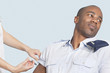 Photo: Young military man looking away as being injected by nurse over light blue background Young military man looking away as being injected by nurse over light blue background