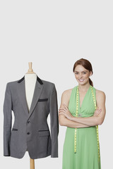 Photo: Portrait of female dressmaker standing next to tailor's dummy over gray background Portrait of female dressmaker standing next to tailor's dummy over gray background