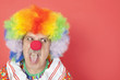 Foto: Senior male clown sticking out tongue while looking away over red background Senior male clown sticking out tongue while looking away over red background