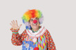 Foto: Cheerful senior male clown waving hand while looking away over gray background Cheerful senior male clown waving hand while looking away over gray background