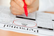 Hand with Red Pen Checking Personals in Newspaper