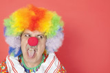 Foto: Senior male clown sticking out tongue while looking away over red background Senior male clown sticking out tongue while looking away over red background