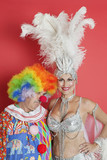 Photo: Portrait of happy senior showgirl with sad clown standing against red background Portrait of happy senior showgirl with sad clown standing against red background