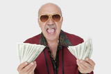 Photo: Portrait of excited senior man showing US banknotes with mouth open against gray background Portrait of excited senior man showing US banknotes with mouth open against gray background
