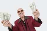 Photo: Portrait of cheerful senior man showing US banknotes against gray background Portrait of cheerful senior man showing US banknotes against gray background