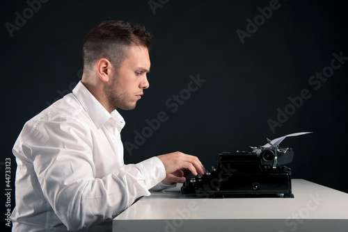 Photo: Young man writing with an old typewriter. Retro image Young man writing with an old typewriter. Retro image