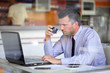 Photo: Authentic image of a businessman drinking coffee while working i Authentic image of a businessman drinking coffee while working i