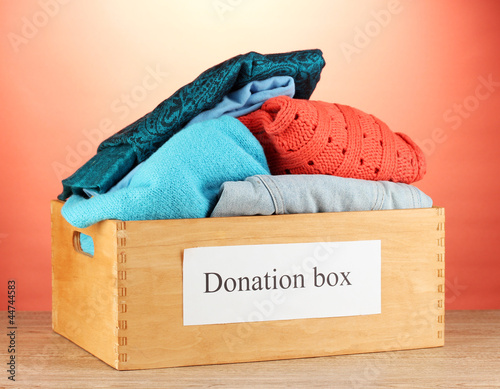Photo: Donation box with clothing on red background close-up Donation box with clothing on red background close-up