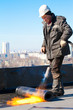 Roofer installing a roll of roofing felt by gas blowpipe torch
