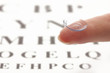 contact lens on finger, on snellen eye chart background