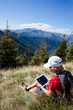 Boy sitting in a mountain meadow using a tablet computer
