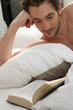 young man bare-chested reading in bed
