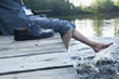 Close-up of young businessman sitting on pier at lake with feet in the water