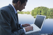 Young businessman using laptop near lake