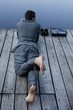 Young businessman lying on pier at lake using laptop