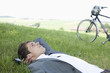 Young businessman lying in grass relaxing near bicycle
