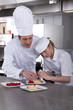 Chef teaching trainee how to garnish gourmet dessert in commercial kitchen