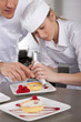 Chef teaching trainee how to garnish gourmet dessert in commercial kitchen