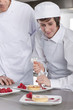 Photo: Chef teaching trainee how to garnish gourmet dessert in commercial kitchen Chef teaching trainee how to garnish gourmet dessert in commercial kitchen