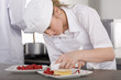Trainee chef wiping plate of gourmet dessert in commercial kitchen