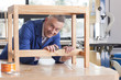 Carpenter in woodshop putting stain on wooden table