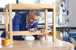 Carpenter in woodshop putting stain on wooden table