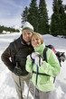 Portrait of happy senior couple backpacking with ski poles in snow