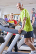 Portrait of personal trainer and smiling senior man exercising on treadmill in gym