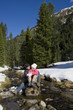 Smiling couple hugging on rock in stream in snowy woods
