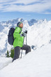 Senior man with backpack and ski poles trekking up slope on snowy mountain