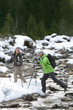Couple with ski poles crossing stream in snowy woods
