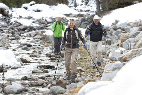 Photo: Smiling seniors with ski poles walking along stream Smiling seniors with ski poles walking along stream