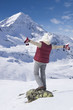 Senior woman standing with arms outstretched on rock on snowy mountain