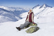 Smiling senior woman sitting with eyes closed on rock on snowy mountain