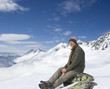 Smiling senior man sitting on rock on snowy mountain