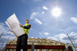 Sun in blue sky over architect holding blueprints at construction site