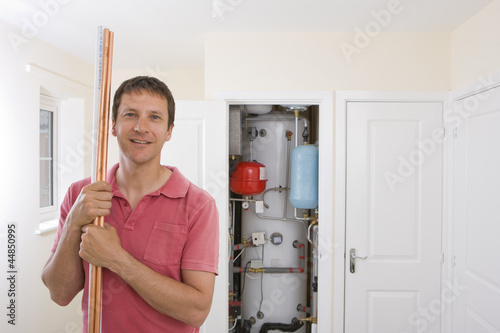 Photo: Portrait of smiling man with copper pipes in front of boiler in closet Portrait of smiling man with copper pipes in front of boiler in closet