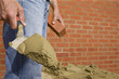 Close up of bricklayer holding mortar on trowel in front of brick wall