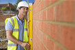 Bricklayer holding level tool against brick wall