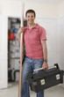 Photo: Portrait of smiling handyman holding toolbox and copper pipes in front of boiler in closet Portrait of smiling handyman holding toolbox and copper pipes in front of boiler in closet