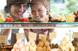 Couple looking at food on display in bakery, view through glass