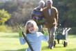 Portrait of smiling girl with gardening gloves and hoe in garden with grandparents in background