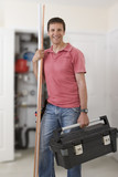 Photo: Portrait of smiling handyman holding toolbox and copper pipes in front of boiler in closet Portrait of smiling handyman holding toolbox and copper pipes in front of boiler in closet