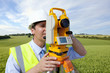 Close up of surveyor looking through theodolite in rural field