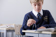 Photo: Male student in school uniform using drawing compass at desk in classroom Male student in school uniform using drawing compass at desk in classroom